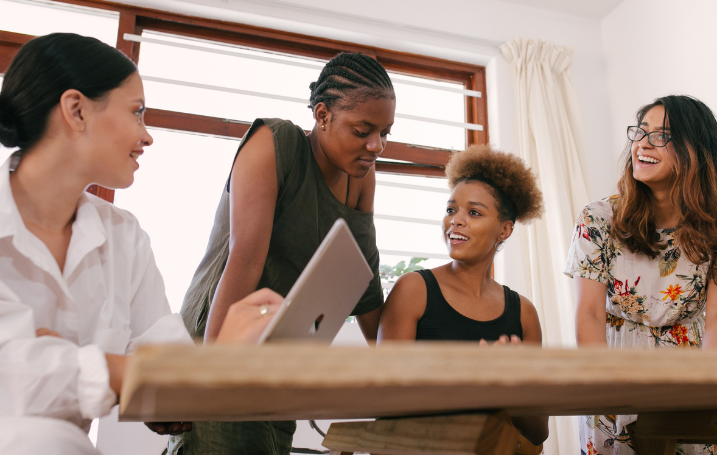 Four women of colour sitting round a table with a laptop having an animated discussion